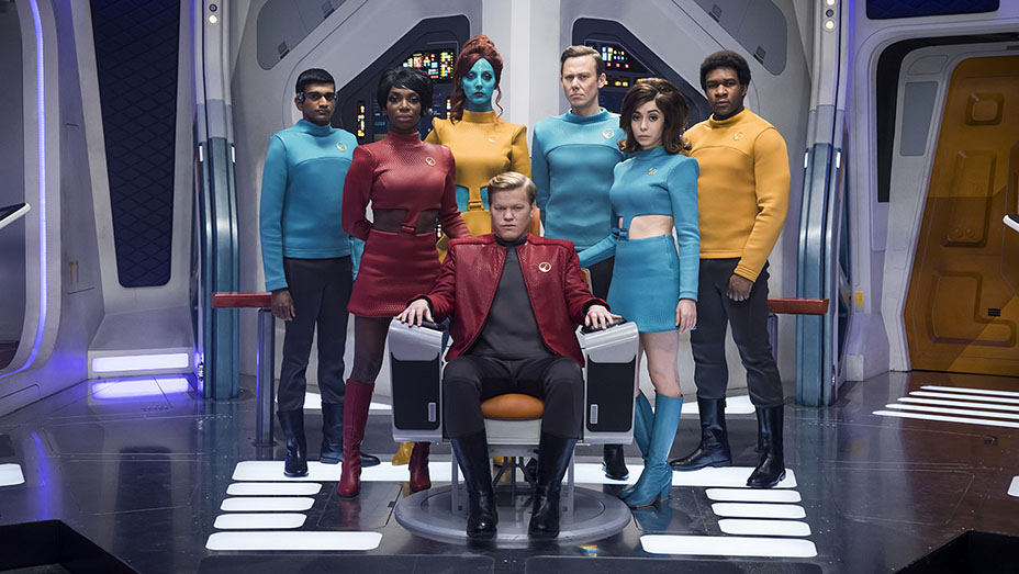 Robert Daly, the captain of USS Callister in 'Black Mirror', sits authoritatively in the captain's chair, surrounded by his attentive crew who look ahead, symbolizing his control and the crew's unity.